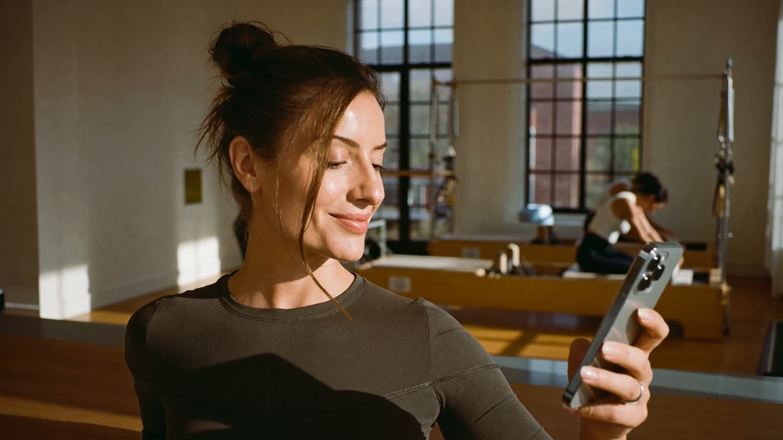 Pilates stüdyosunda telefonuna bakıp gülümseyen eğitmen